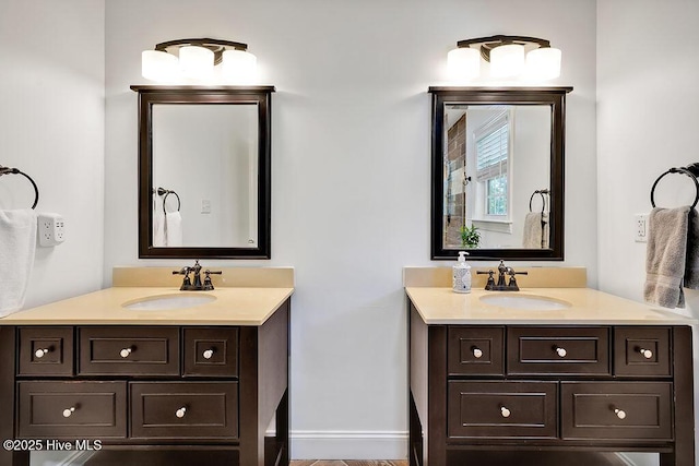 bathroom featuring a sink, two vanities, and baseboards