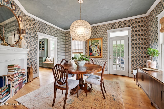 dining space with a notable chandelier, crown molding, light wood-style flooring, and wallpapered walls