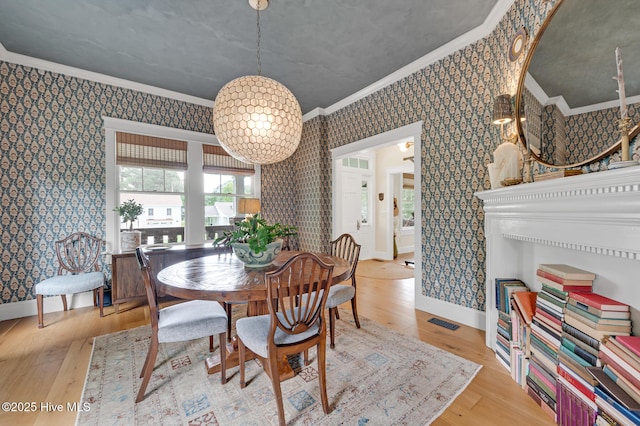 dining space featuring wood finished floors, ornamental molding, visible vents, baseboards, and wallpapered walls