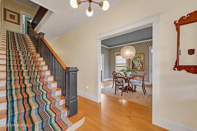 staircase with baseboards, ornamental molding, an inviting chandelier, and wood finished floors