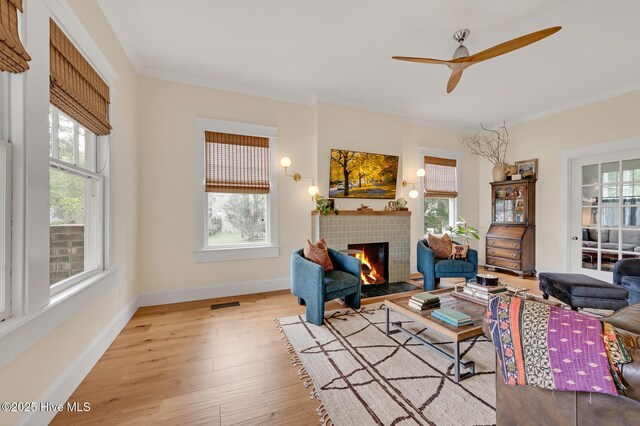 living room featuring ceiling fan, crown molding, a fireplace, and a healthy amount of sunlight