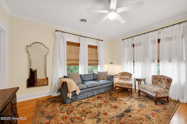 living area featuring wood finished floors, ornamental molding, visible vents, a ceiling fan, and baseboards
