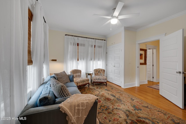 living room featuring ceiling fan, ornamental molding, baseboards, and wood finished floors