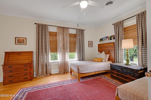 bedroom with wood finished floors, a ceiling fan, visible vents, baseboards, and ornamental molding
