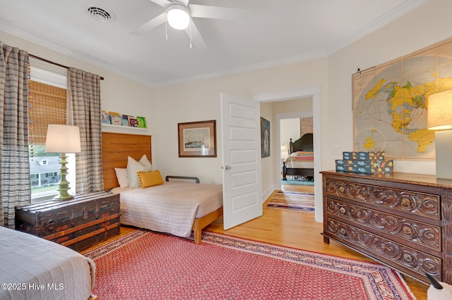 bedroom featuring ceiling fan, ornamental molding, visible vents, and wood finished floors