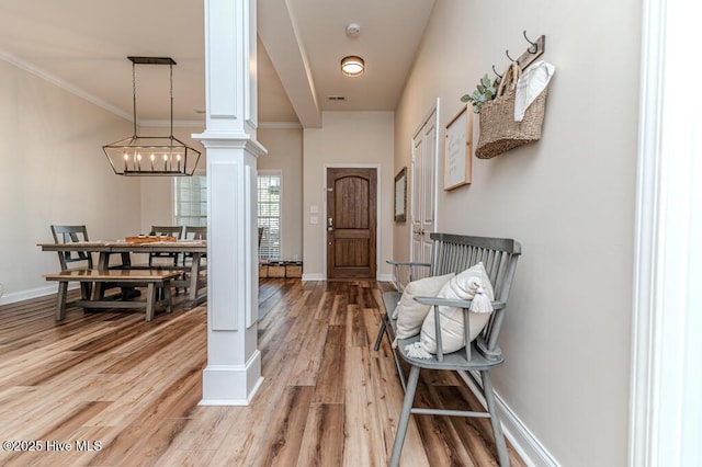 entryway with decorative columns, light wood finished floors, ornamental molding, and baseboards