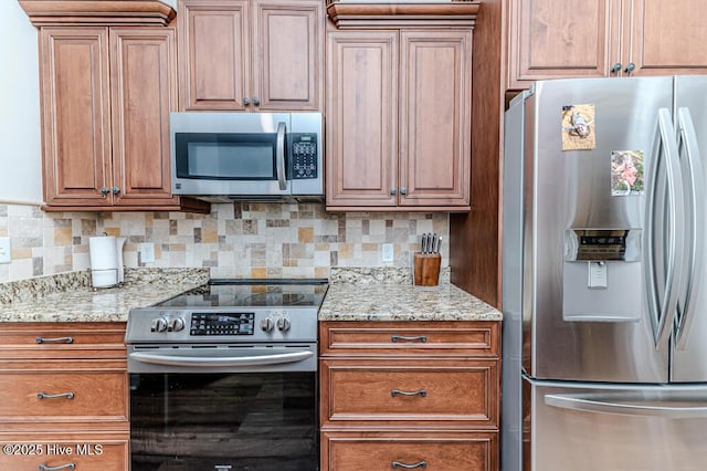 kitchen with appliances with stainless steel finishes, tasteful backsplash, brown cabinetry, and light stone counters