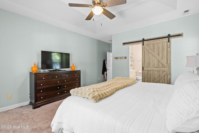 4145 Brighton Ln, Southport, NC 28461 - carpeted bedroom with a tray ceiling, a barn door, baseboards, ensuite bath, and visible vents