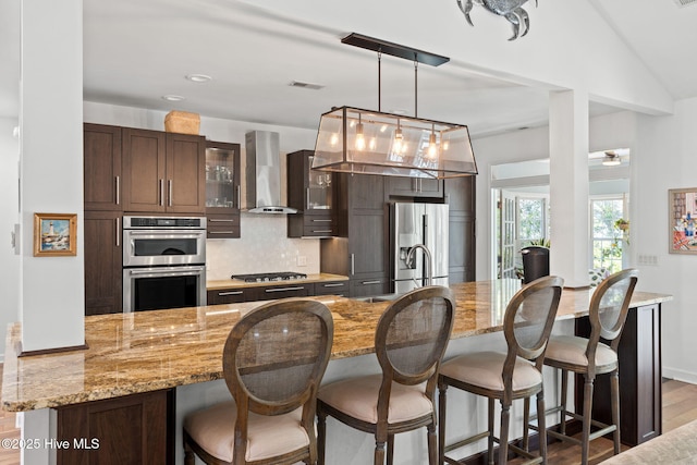 4145 Brighton Ln, Southport, NC 28461 - kitchen with stainless steel appliances, wall chimney exhaust hood, a kitchen bar, decorative backsplash, and dark brown cabinets