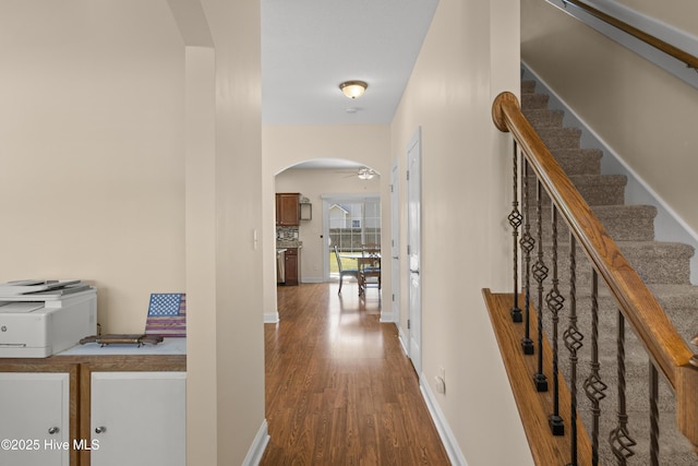 hall with arched walkways, wood finished floors, baseboards, and stairway