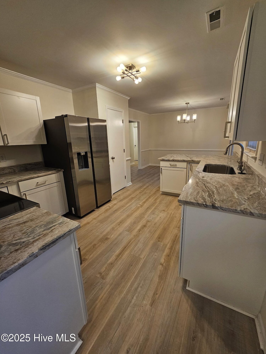 kitchen with a sink, light wood-type flooring, stainless steel refrigerator with ice dispenser, white cabinets, and a notable chandelier