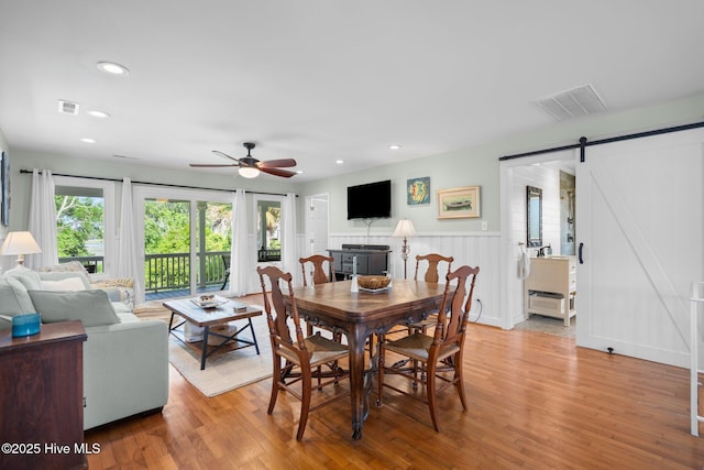 dining space featuring a barn door, light wood-style flooring, ceiling fan, recessed lighting, and a wainscoted wall