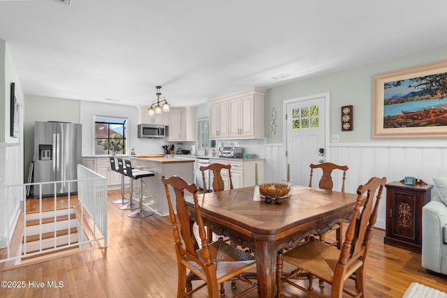 dining space featuring a wainscoted wall, light wood-style floors, and a chandelier