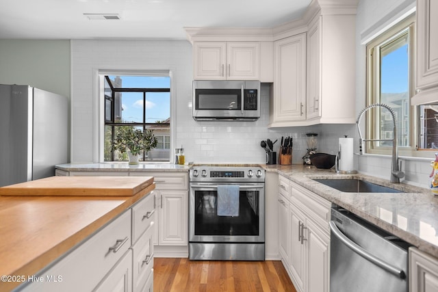 kitchen featuring appliances with stainless steel finishes, a sink, white cabinetry, and backsplash