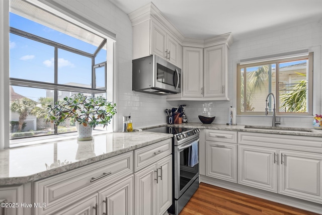 kitchen with appliances with stainless steel finishes, a sink, white cabinets, decorative backsplash, and wood finished floors