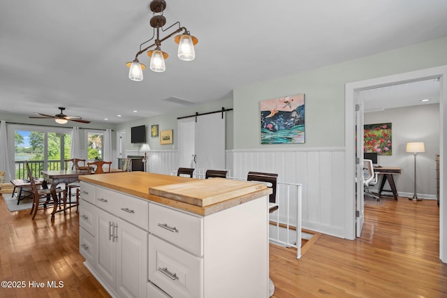 kitchen with wood counters, a barn door, ceiling fan, a wainscoted wall, and white cabinets