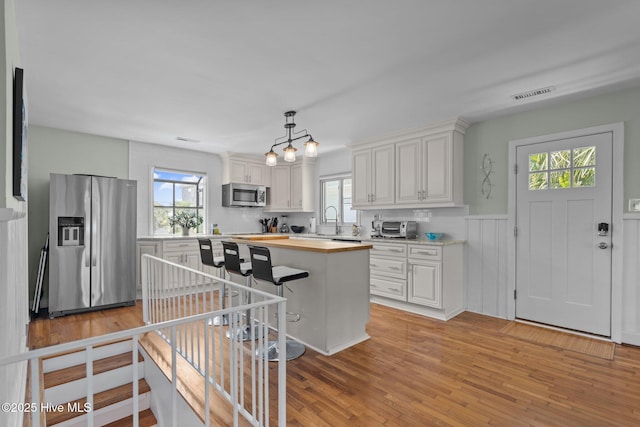 kitchen featuring appliances with stainless steel finishes, butcher block countertops, healthy amount of natural light, and a wainscoted wall