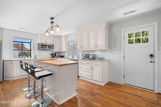 kitchen with stainless steel appliances, butcher block countertops, white cabinets, light wood finished floors, and wainscoting