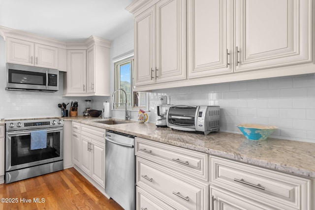 kitchen featuring stainless steel appliances, a sink, tasteful backsplash, and white cabinets