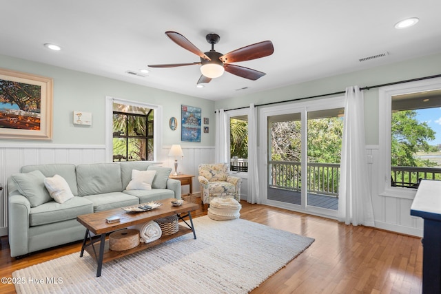 living room featuring wainscoting, wood finished floors, ceiling fan, a decorative wall, and recessed lighting