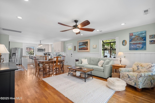 living room featuring a ceiling fan, a wainscoted wall, plenty of natural light, light wood-style flooring, and recessed lighting