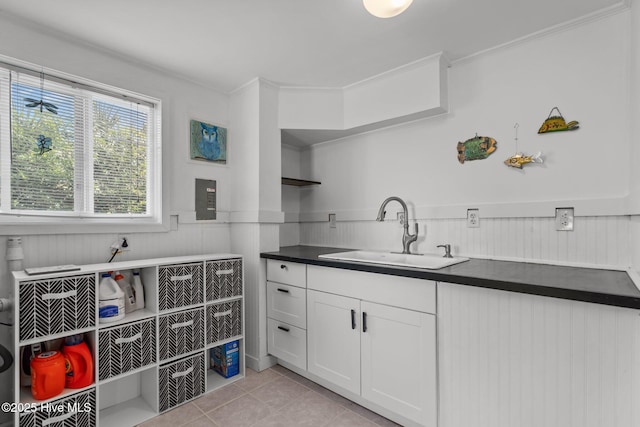 kitchen featuring a sink, wainscoting, light tile patterned floors, white cabinetry, and dark countertops
