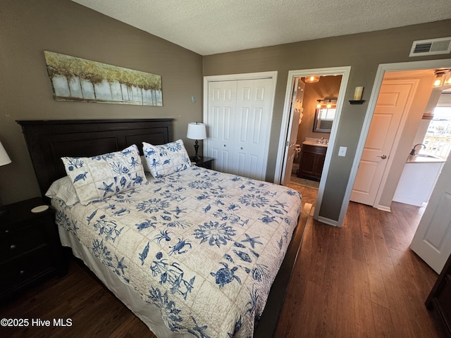 bedroom with dark wood-style floors, a closet, a textured ceiling, ensuite bath, and baseboards