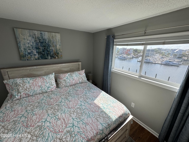 bedroom with wood finished floors, a water view, a textured ceiling, and baseboards