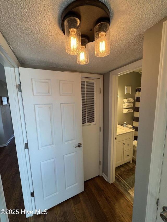 hallway with dark wood-type flooring, a textured ceiling, and baseboards