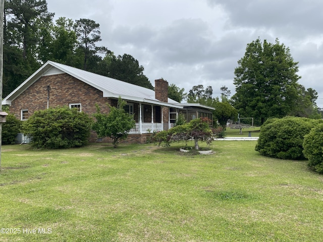 view of home's exterior with a chimney, a lawn, brick siding, and covered porch