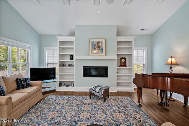 living area featuring vaulted ceiling, wood finished floors, a glass covered fireplace, and a ceiling fan