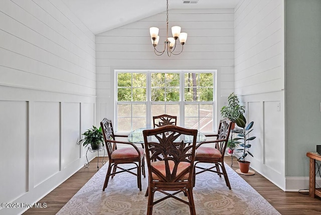 dining space with high vaulted ceiling, a chandelier, dark wood-style flooring, and a decorative wall