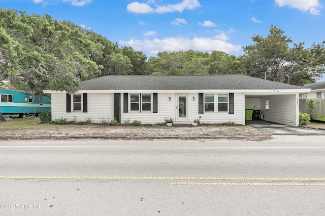ranch-style house with concrete driveway, a carport, and roof with shingles
