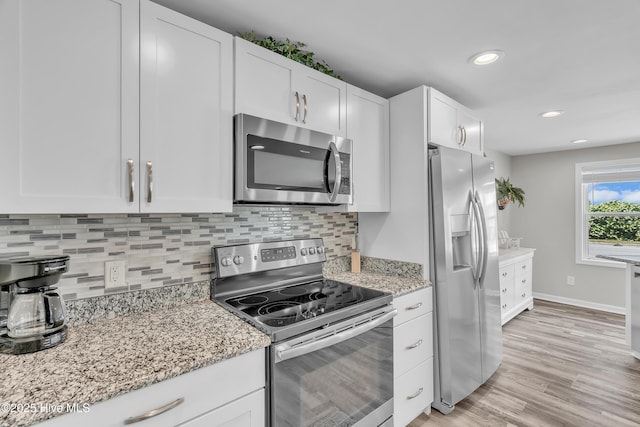 kitchen with stainless steel appliances, white cabinets, backsplash, light stone counters, and light wood-style flooring
