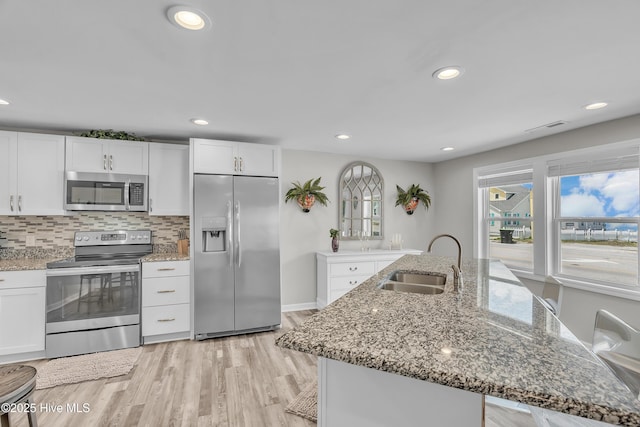 kitchen with appliances with stainless steel finishes, a sink, white cabinetry, light wood-style floors, and light stone countertops