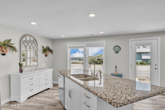 kitchen featuring a sink, dishwashing machine, light wood finished floors, light stone countertops, and white cabinetry