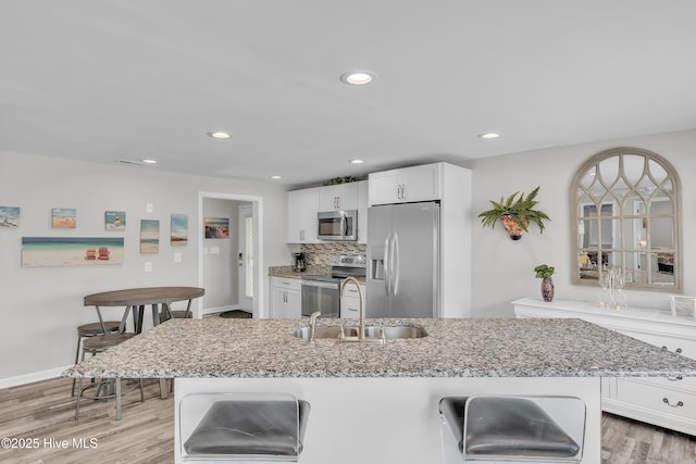 kitchen with stainless steel appliances, a sink, a kitchen bar, light stone countertops, and white cabinetry