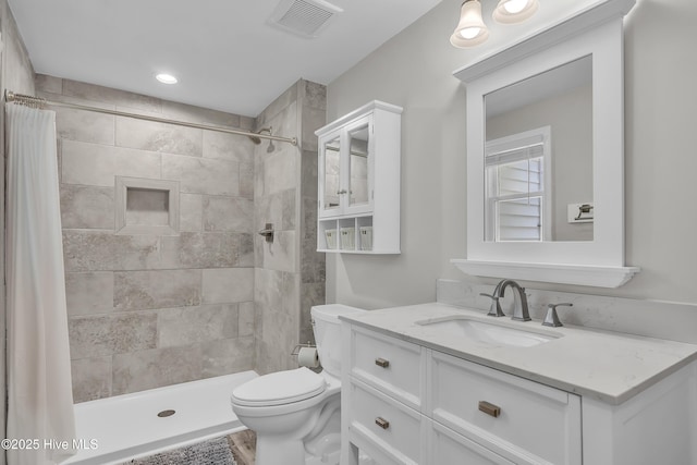 bathroom with toilet, tiled shower, and vanity