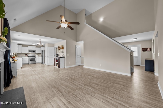 unfurnished living room featuring ceiling fan with notable chandelier, high vaulted ceiling, visible vents, light wood-style flooring, and baseboards