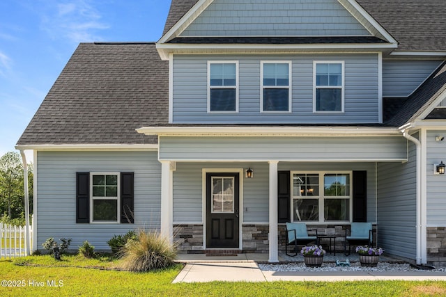 craftsman-style home featuring roof with shingles, covered porch, and fence