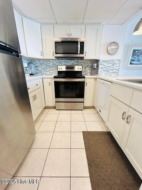kitchen with appliances with stainless steel finishes, white cabinets, light countertops, tasteful backsplash, and light tile patterned flooring