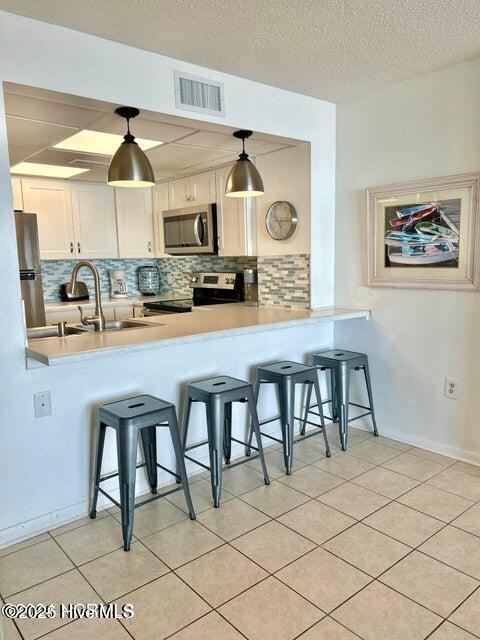 kitchen featuring appliances with stainless steel finishes, a peninsula, tasteful backsplash, a kitchen breakfast bar, and a textured ceiling