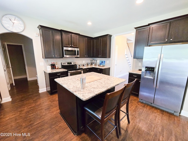 kitchen featuring dark brown cabinetry, stainless steel appliances, tasteful backsplash, and arched walkways