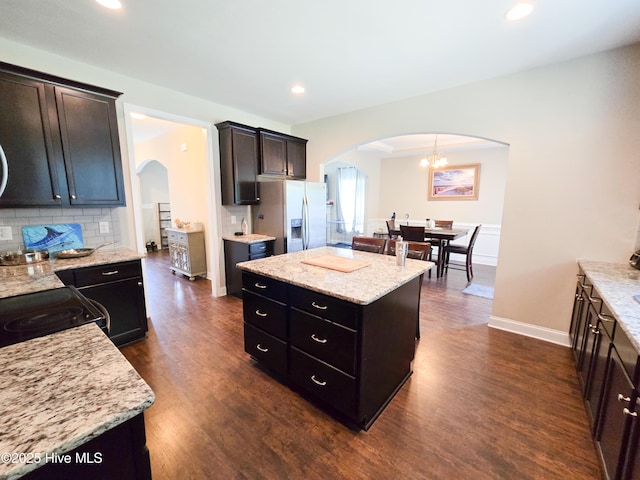 kitchen with arched walkways, stainless steel fridge with ice dispenser, a center island, and dark wood-style floors