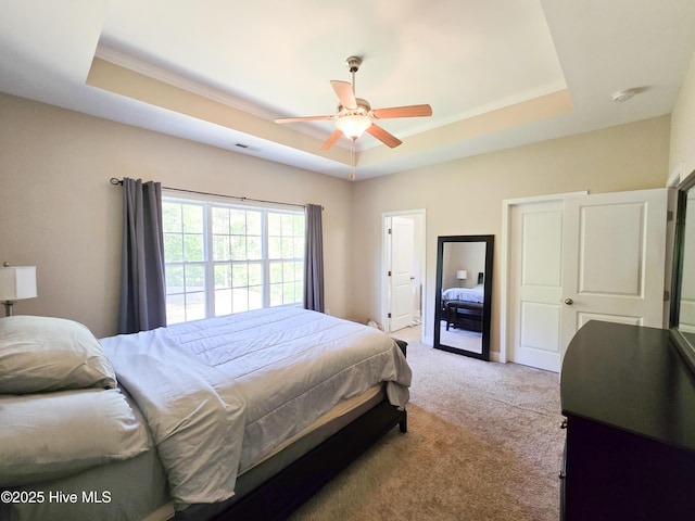 bedroom with a tray ceiling, visible vents, ceiling fan, light colored carpet, and ornamental molding