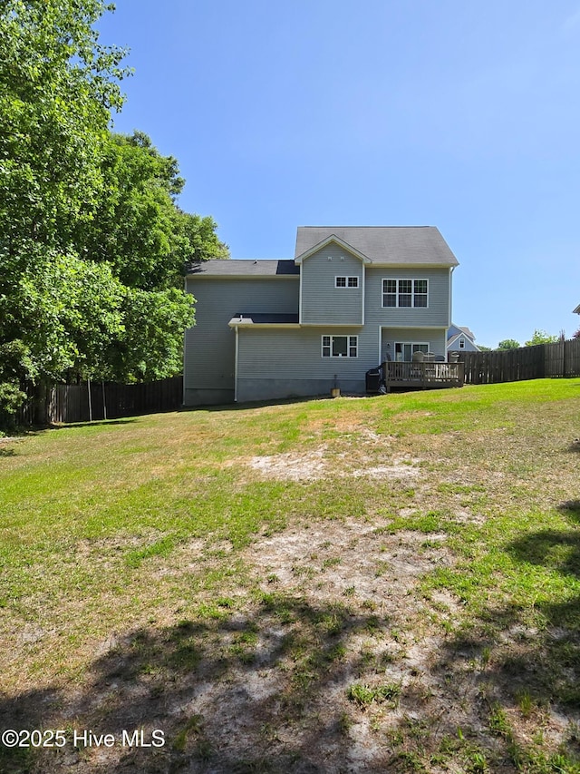 back of property with fence, a wooden deck, and a lawn