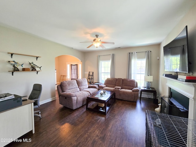 living room featuring a fireplace, arched walkways, a ceiling fan, and wood finished floors