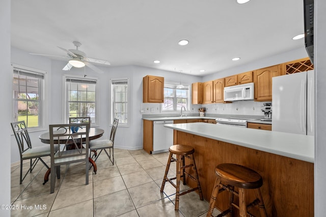 kitchen featuring white appliances, a sink, light countertops, a breakfast bar area, and baseboards