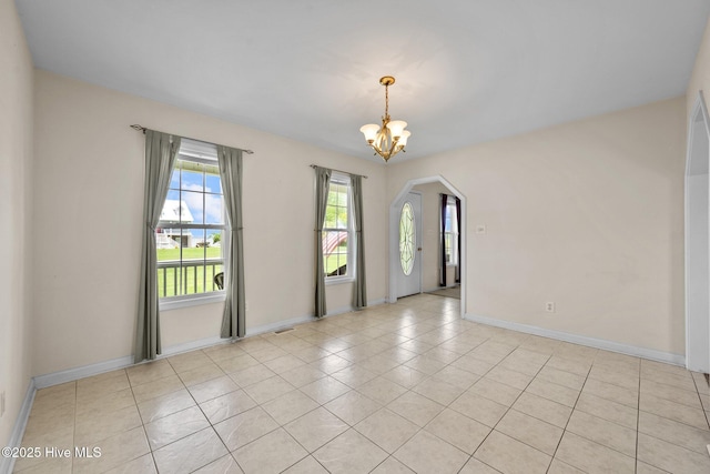 unfurnished room with arched walkways, a chandelier, light tile patterned floors, and baseboards