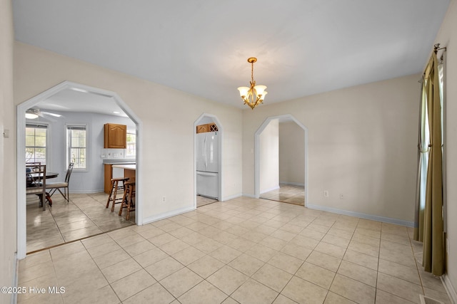 unfurnished room with arched walkways, light tile patterned floors, baseboards, and a chandelier